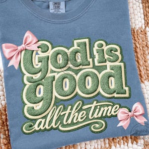 May include: A blue Comfort Colors t-shirt featuring the text "God is good all the time" in green and cream. Two pink bows are attached to the shirt. The t-shirt has a crew neck and is made of a soft material.