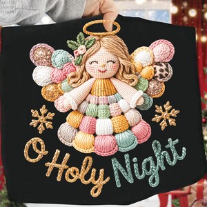 May include: Black fabric Christmas decoration featuring a crocheted angel with a gold halo and colorful yarn wings and dress. The words "O Holy Night" are embroidered in gold and teal. Two gold snowflakes are also embroidered on the fabric.