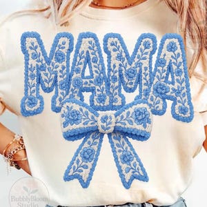 May include: Cream-colored t-shirt featuring the word "MAMA" in blue floral embroidery, with a matching bow design below. The design has a textured, three-dimensional appearance, creating a visually appealing and stylish look. The shirt is a casual wear item.