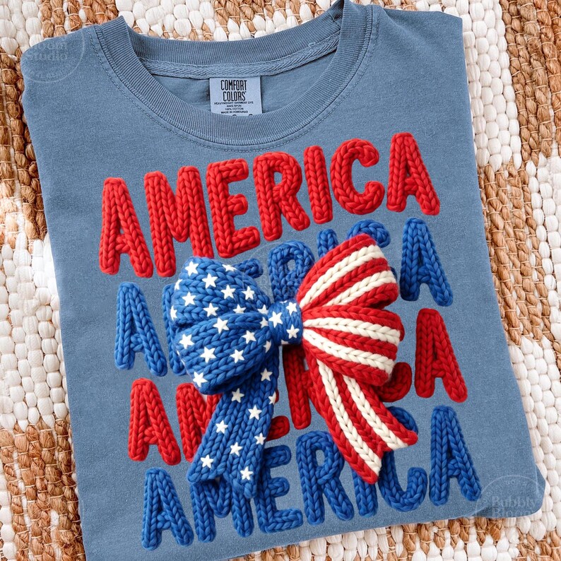 May include: A blue t-shirt with the word "AMERICA" in red, white, and blue knitted letters. A bow with a star-spangled blue section and red and white stripes is centered on the shirt. The shirt is a Comfort Colors brand.