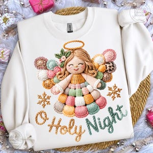 May include: White sweatshirt featuring a colorful angel design with a halo, wings, and the text "O Holy Night." The angel is made of yarn in various colors. Two gold snowflakes are also present.