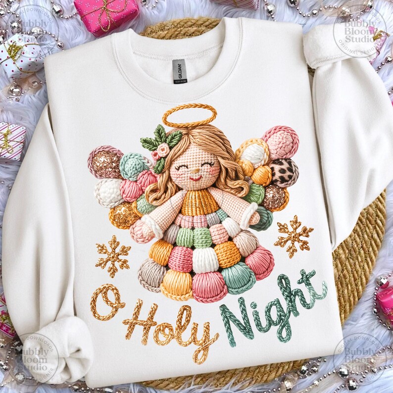 May include: White sweatshirt featuring a colorful angel design with a halo, wings, and the text "O Holy Night." The angel is made of yarn in various colors. Two gold snowflakes are also present.