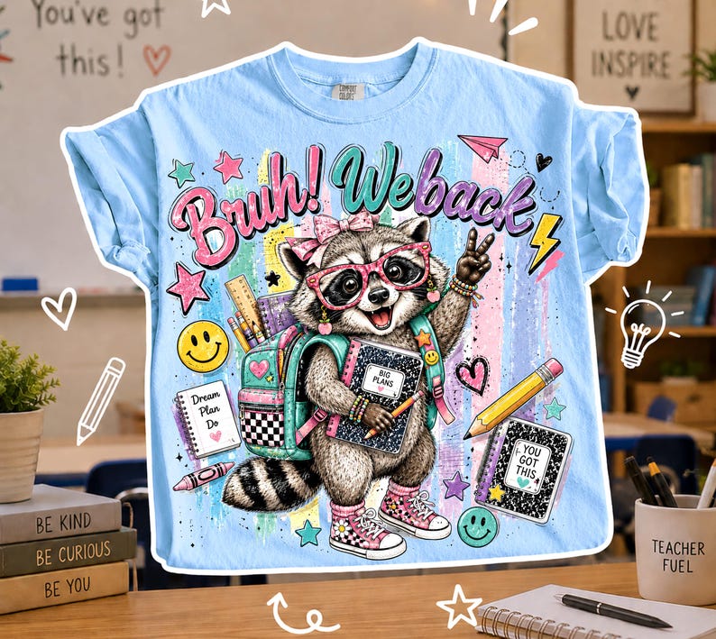Puede incluir: Camiseta azul claro con un gr&aacute;fico de mapache con gafas y una mochila, sosteniendo un cuaderno. La camiseta tiene el texto "Bruh! Weback" y gr&aacute;ficos escolares. La camiseta est&aacute; sobre una mesa de madera.