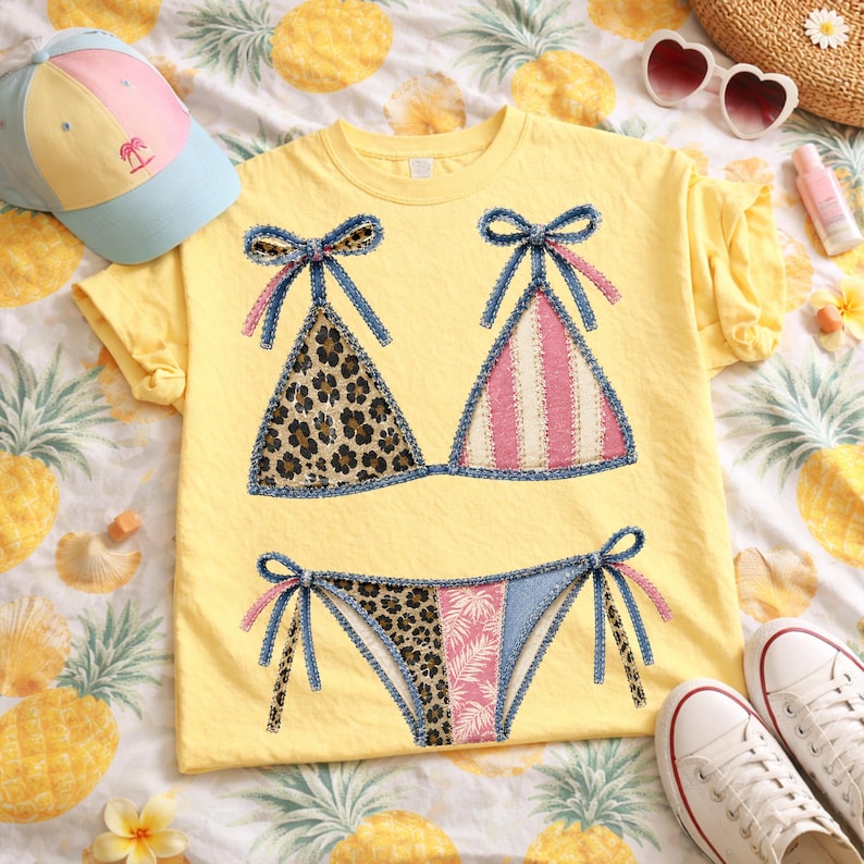 May include: Yellow t-shirt with a bikini design. The bikini top features leopard print and pink stripes, with denim-like bows. The matching bikini bottom has leopard print and a pink floral pattern. A light blue and pink cap and white sneakers are also visible.