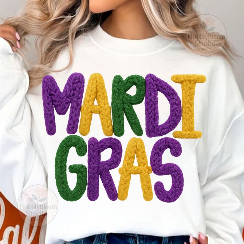 May include: White sweatshirt with the words "MARDI GRAS" in large, textured letters. The letters are in purple, yellow, and green, with a knitted appearance. The design is centered on the front of the shirt.