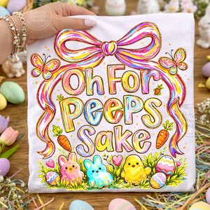 May include: White t-shirt with a colorful Easter design. The shirt features the phrase "Oh For Peeps Sake" in rainbow lettering, along with illustrations of bunnies, a chick, carrots, butterflies, and Easter eggs. A large rainbow bow tops the design.