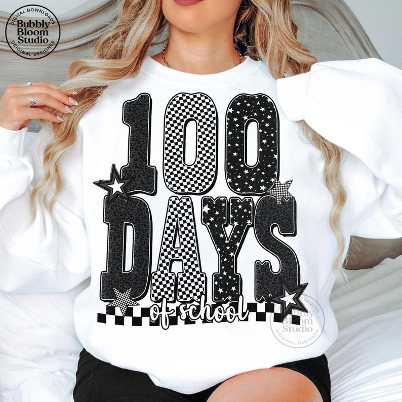May include: White sweatshirt with a large graphic that reads "100 DAYS of school." The numbers and letters are black and white, with checkered, star, and leopard print patterns. The design includes star accents.