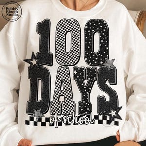 May include: White sweatshirt with a black and white graphic that reads "100 DAYS of school." The numbers and letters have various patterns, including leopard print, checkered, and stars. The design includes star accents.