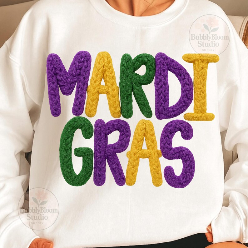 May include: White sweatshirt with the words "MARDI GRAS" in textured, colorful letters. The letters are purple, green, and yellow, with a knitted appearance. The design is centered on the chest.