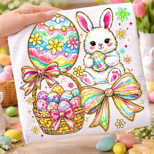 May include: A white Easter-themed design featuring a bunny holding an egg, a basket of decorated eggs, and a large decorated egg. The design includes colorful bows, flowers, and gold glitter accents. The image is on a white background.
