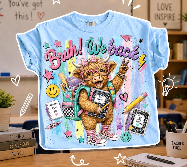 以下が含まれることがあります： メガネ、バックパック、スニーカーを履いたハイランド牛のグラフィックが描かれた水色のTシャツ。「Bruh! We back」の文字が牛の上にあります。鉛筆、ノート、スマイリーフェイスなど、学校をテーマにしたグラフィックが描かれています。「You've got this!」の文字が上にあります。