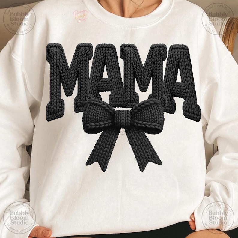 May include: White sweatshirt with the word "MAMA" in large, black, knitted letters. A black knitted bow is centered below the word. The sweatshirt is a casual style.