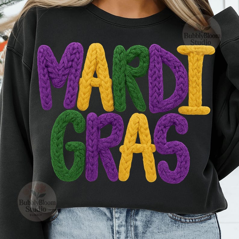 May include: Black sweatshirt with the words "MARDI GRAS" in large, textured letters. The letters are in purple, yellow, and green, with a knitted appearance. The sweatshirt is a casual style.
