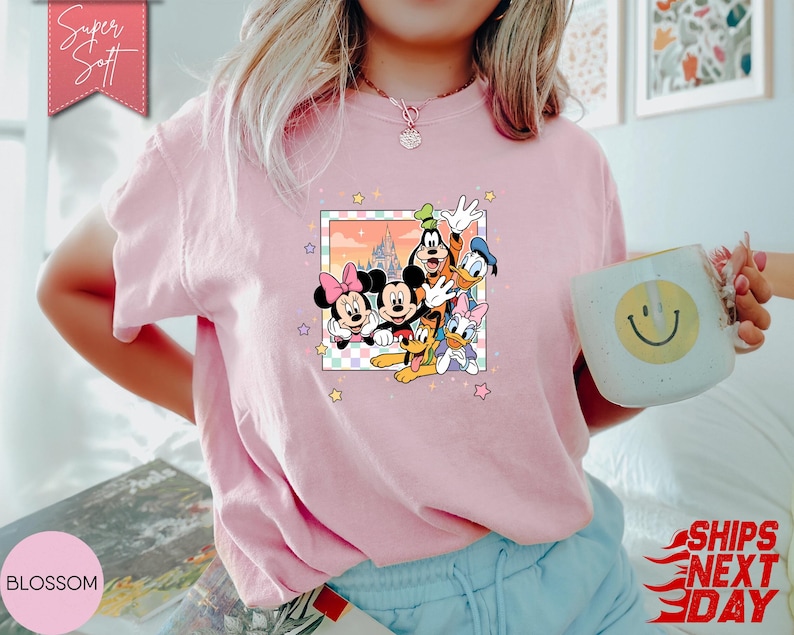 Może przedstawiać: Jasnor&oacute;żowa koszulka z kolorową grafiką postaci Disneya: Myszki Miki, Myszki Minnie, Goofy'ego, Kaczora Donalda i Daisy Duck. Koszulka ma okrągły dekolt i kr&oacute;tkie rękawy. Napis "Super Soft" znajduje się na r&oacute;żowym banerze.