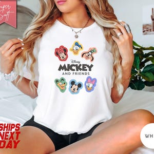 May include: White t-shirt featuring the text "Mickey and Friends" with colorful cartoon character graphics. The shirt has a crew neck and short sleeves. The design includes Mickey Mouse, Minnie Mouse, Donald Duck, Daisy Duck, and Goofy.