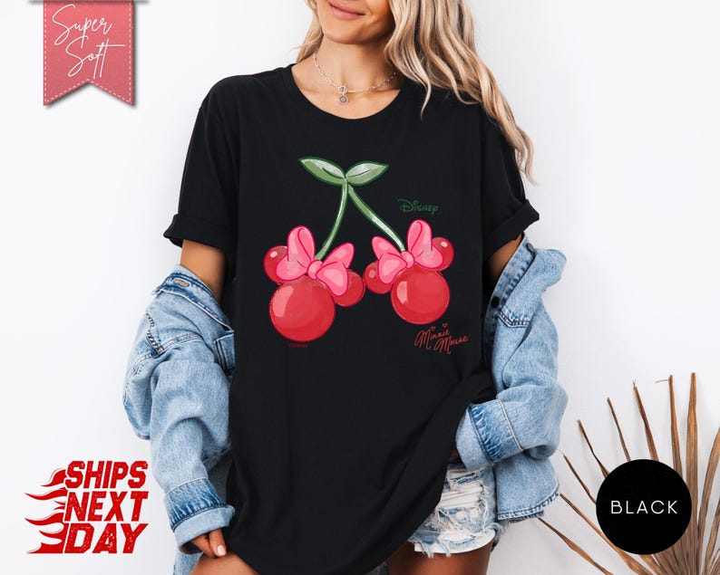 May include: Black t-shirt featuring a Minnie Mouse cherry design. The graphic includes two red cherries with pink bows, green leaves, and the Disney and Minnie Mouse logos. The shirt has short sleeves.