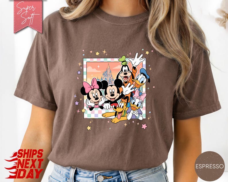 Może przedstawiać: Koszulka w kolorze espresso z kolorową grafiką Myszki Miki, Myszki Minnie, Goofy'ego, Kaczora Donalda, Daisy Duck i Pluto. Grafika jest obramowana pastelową obw&oacute;dką i gwiazdkami. Koszulka ma napis "Super Soft" u g&oacute;ry po lewej.