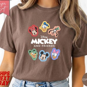 May include: Espresso-colored t-shirt featuring the text "Mickey and Friends" with cartoon character graphics. The shirt has a crew neck and short sleeves. The design includes Mickey Mouse, Minnie Mouse, Donald Duck, Daisy Duck, Goofy, and Pluto.