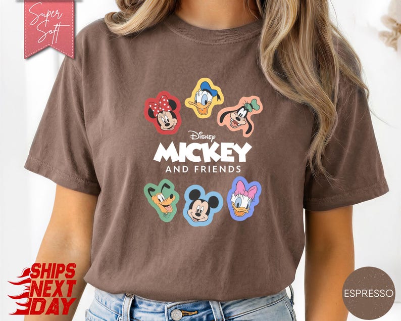 May include: Espresso-colored t-shirt featuring the text "Mickey and Friends" with cartoon character graphics. The shirt has a crew neck and short sleeves. The design includes Mickey Mouse, Minnie Mouse, Donald Duck, Daisy Duck, Goofy, and Pluto.