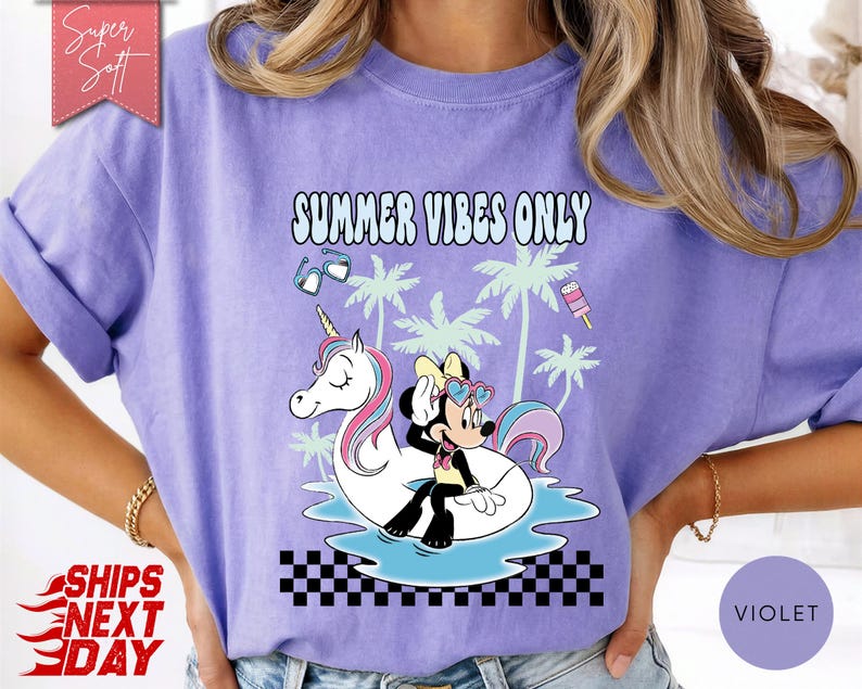 May include: A light purple t-shirt featuring a graphic print of Minnie Mouse sitting on a white unicorn pool float in blue water. The design includes palm trees, sunglasses, a popsicle, and the text SUMMER VIBES ONLY above a black and white checkerboard pattern.
