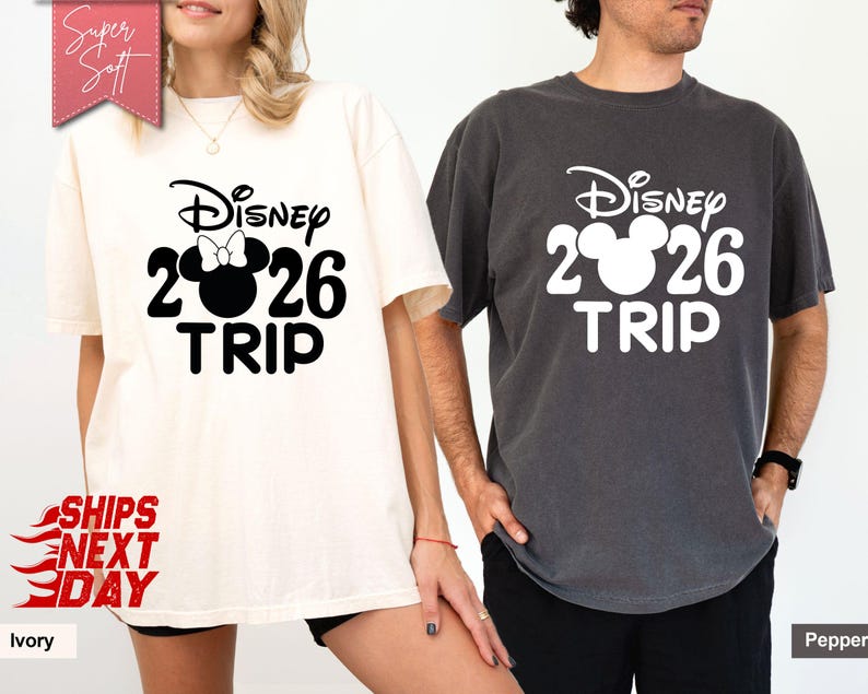 May include: Two short-sleeved t-shirts, one ivory and one pepper, featuring a Disney design. The design includes the word "Disney", the number "2026", a Mickey Mouse head, and the word "TRIP" in a bold, black font. The ivory shirt has a bow on the Mickey Mouse head.