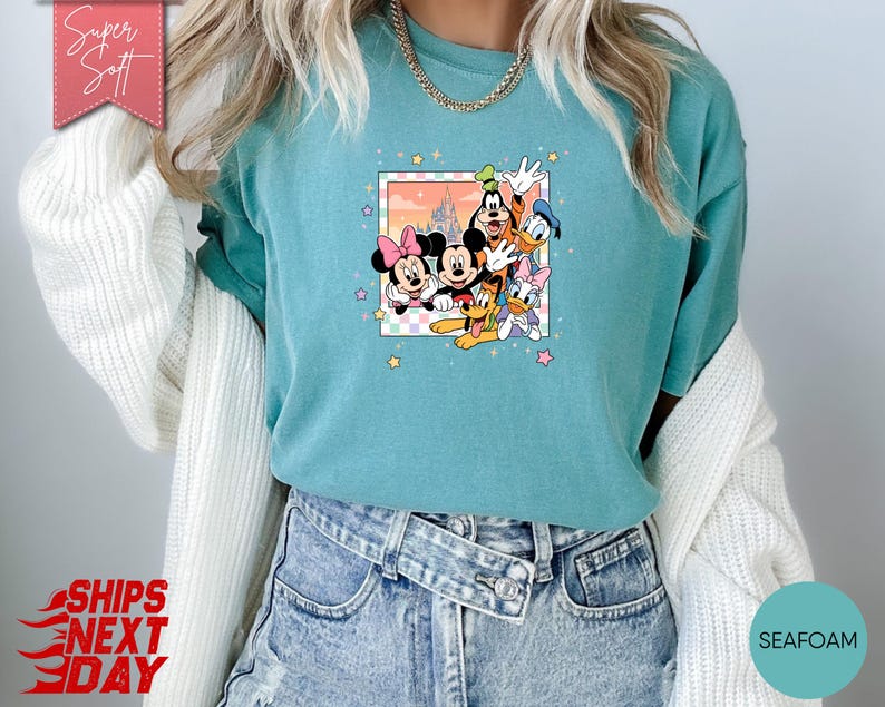 Może przedstawiać: Turkusowa koszulka z kolorową grafiką postaci Disneya: Myszki Miki, Myszki Minnie, Kaczora Donalda, Kaczki Daisy, Goofy'ego i Plutona. Grafika jest obramowana jasnor&oacute;żową i białą szachownicą oraz tłem zachodu słońca. Koszulka ma napis "Super Soft" na r&oacute;żowym banerze.