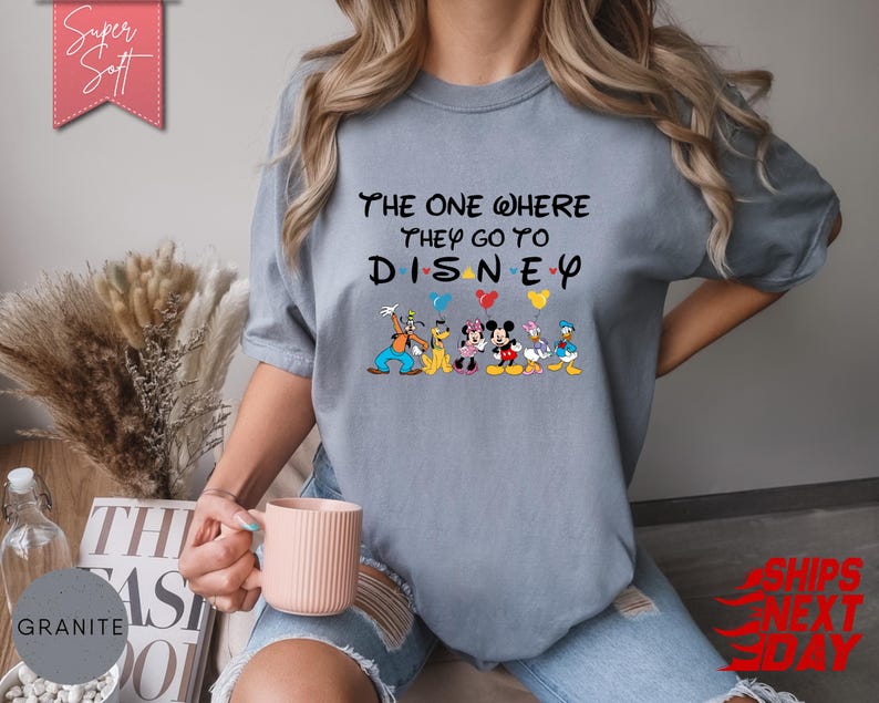 K&ouml;nnte beinhalten: Ein hellblaues T-Shirt mit dem Text "The One Where They Go To Disney" und Disney-Figuren. Das Shirt hat einen Rundhalsausschnitt und kurze &Auml;rmel. Das Design umfasst Micky Maus, Minnie Maus, Donald Duck und Goofy.