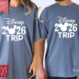 May include: Two blue jean-colored t-shirts with the text "Disney 2026 TRIP" in white. One shirt features a Minnie Mouse bow in the "2" of 2026. The shirts are short-sleeved and have a relaxed fit.