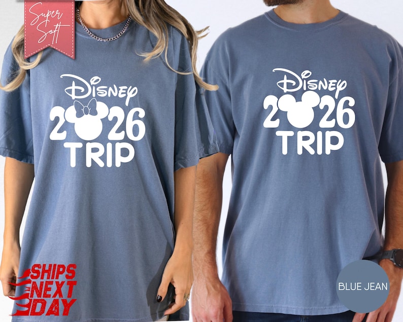 May include: Two blue jean-colored t-shirts with the text "Disney 2026 TRIP" in white. One shirt features a Minnie Mouse bow in the "2" of 2026. The shirts are short-sleeved and have a relaxed fit.