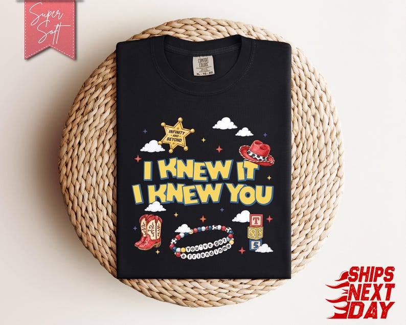 May include: A black t-shirt featuring a graphic print with the text I KNEW IT I KNEW YOU in yellow letters. The design includes a gold sheriff star, a red cowboy hat, red cowboy boots, a beaded bracelet with the text YOU'VE GOT A FRIEND IN ME.
