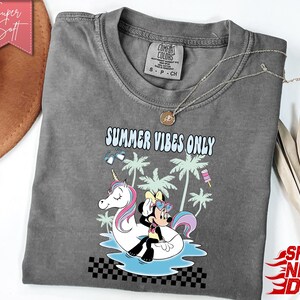 May include: A charcoal gray short-sleeve t-shirt featuring a graphic print of a cartoon mouse and a unicorn on a pool float. The text reads SUMMER VIBES ONLY. The design includes palm trees, heart-shaped sunglasses, and a popsicle, with a black and white checkered pattern at the bottom.