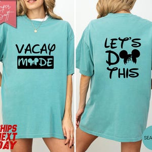 May include: Seafoam green t-shirt with black text and graphics. The front of the shirt says "VACAY MODE" with a Mickey Mouse head graphic. The back says "LET'S DO THIS" with a Mickey Mouse head graphic. The shirt is a relaxed fit.