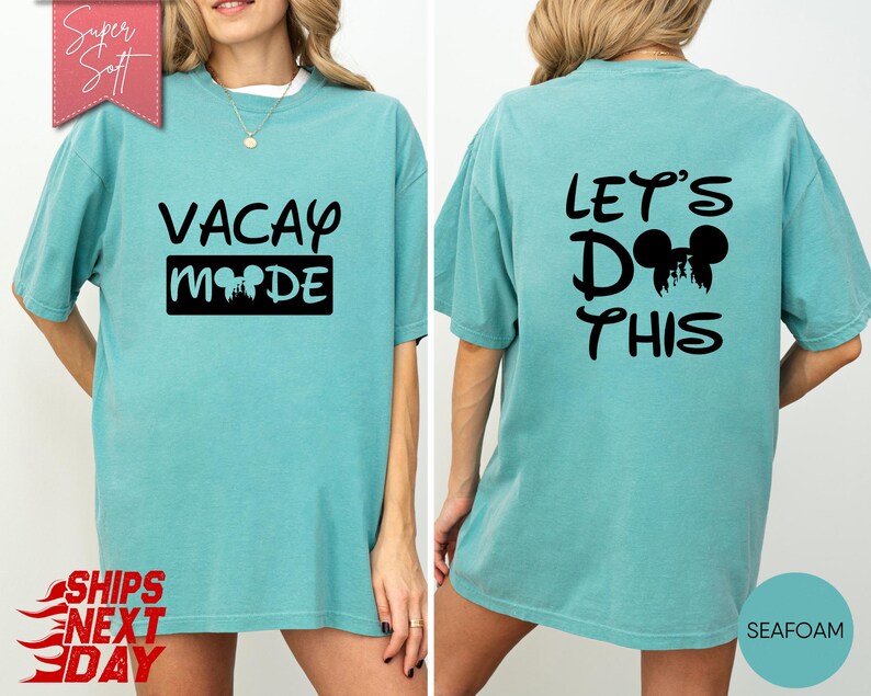 May include: Seafoam green t-shirt with black text and graphics. The front of the shirt says "VACAY MODE" with a Mickey Mouse head graphic. The back says "LET'S DO THIS" with a Mickey Mouse head graphic. The shirt is a relaxed fit.