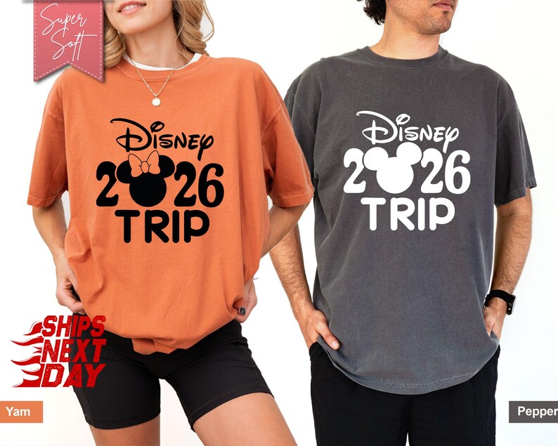 May include: Two short-sleeved t-shirts, one orange and one gray, each with a Disney design. The design includes the Disney logo, the number 2026, and the word "TRIP". The orange shirt has a Minnie Mouse bow.