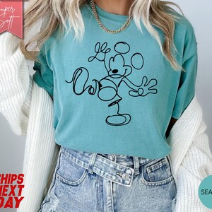 May include: Seafoam green t-shirt featuring a black line drawing of Mickey Mouse with the words "Love" and "Oh" in cursive. The shirt is made of a soft material and has a relaxed fit. The words "Super Soft" are in a pink banner.