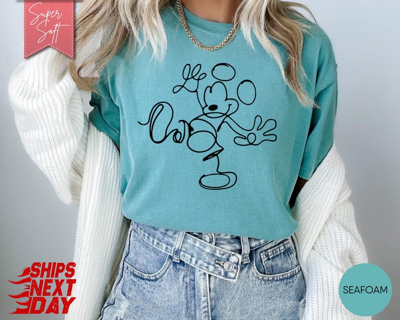 May include: Seafoam green t-shirt featuring a black line drawing of Mickey Mouse with the words "Love" and "Oh" in cursive. The shirt is made of a soft material and has a relaxed fit. The words "Super Soft" are in a pink banner.