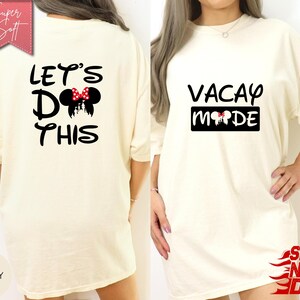 May include: Ivory-colored t-shirt with the text "LET'S DO THIS" and a Minnie Mouse design on the back. The front of the shirt has the text "VACAY MODE" with a Minnie Mouse design. The shirt is a loose fit.