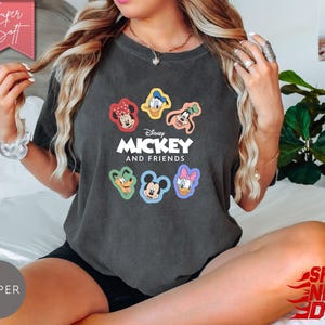 May include: Dark gray t-shirt featuring the text "Mickey and Friends" with colorful character graphics. The shirt has a crew neck and short sleeves. The image also includes the text "Super Soft" and "Ships Next Day".