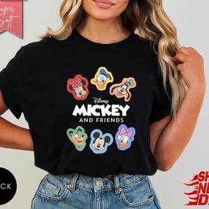 May include: Black t-shirt featuring the text "Disney MICKEY AND FRIENDS" with cartoon character graphics. The shirt includes images of Mickey Mouse, Minnie Mouse, Donald Duck, Daisy Duck, Goofy, and Pluto. The shirt is labeled "Super Soft".