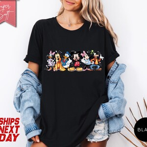 Puede incluir: Camiseta negra con un gr&aacute;fico colorido de personajes de Disney, incluyendo Mickey Mouse, Minnie Mouse, Donald Duck y Goofy. La camiseta tiene el texto "Super Soft" en una pancarta rosa y "Black" en un c&iacute;rculo.