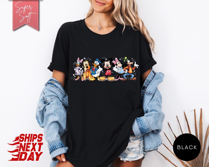 Puede incluir: Camiseta negra con un gr&aacute;fico colorido de personajes de Disney, incluyendo Mickey Mouse, Minnie Mouse, Donald Duck y Goofy. La camiseta tiene el texto "Super Soft" en una pancarta rosa y "Black" en un c&iacute;rculo.