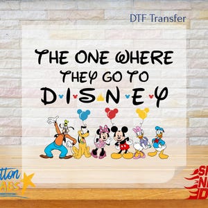 K&ouml;nnte beinhalten: Ein DTF-Transfer mit Disney-Figuren, darunter Goofy, Pluto, Minnie Mouse, Mickey Mouse, Daisy Duck und Donald Duck. Der Text lautet "The One Where They Go To Disney" in schwarzer Schrift. Ballons in Blau, Rot und Gelb sind enthalten.