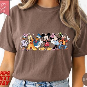 Puede incluir: Camiseta color espresso con un gr&aacute;fico de personajes de Disney: Daisy, Pluto, Donald, Mickey, Minnie y Goofy. La camiseta tiene el texto "Super Soft" y "Ships Next Day".