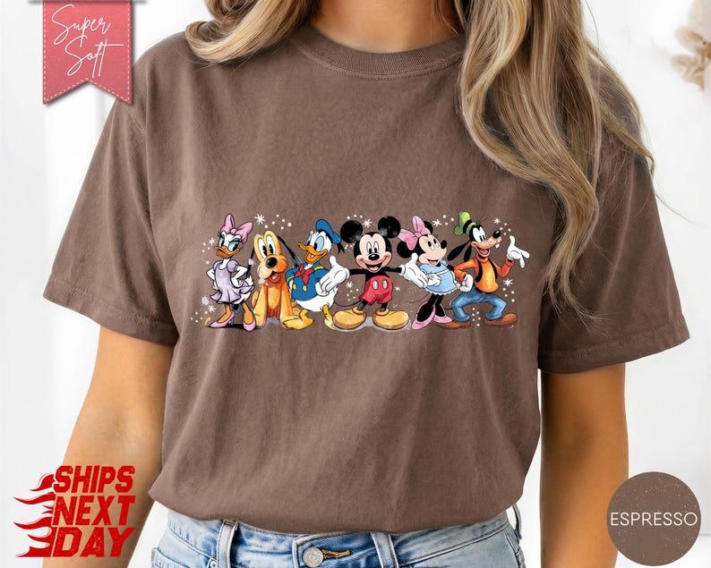 Puede incluir: Camiseta color espresso con un gr&aacute;fico de personajes de Disney: Daisy, Pluto, Donald, Mickey, Minnie y Goofy. La camiseta tiene el texto "Super Soft" y "Ships Next Day".