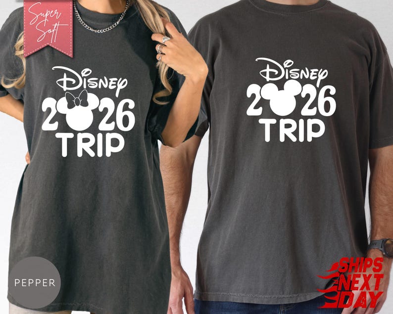 May include: Two dark gray t-shirts with the text "Disney 2026 TRIP" in white. One shirt features a Minnie Mouse bow. The shirts are made of a soft material and are suitable for a Disney vacation.