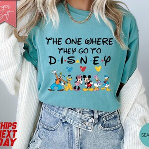 K&ouml;nnte beinhalten: T&uuml;rkisfarbenes T-Shirt mit dem Text "THE ONE WHERE THEY GO TO DISNEY" und Disney-Figuren. Das Shirt zeigt Goofy, Pluto, Minnie Mouse, Mickey Mouse und Donald Duck mit Luftballons. Das Shirt ist aus einem weichen, bequemen Material.