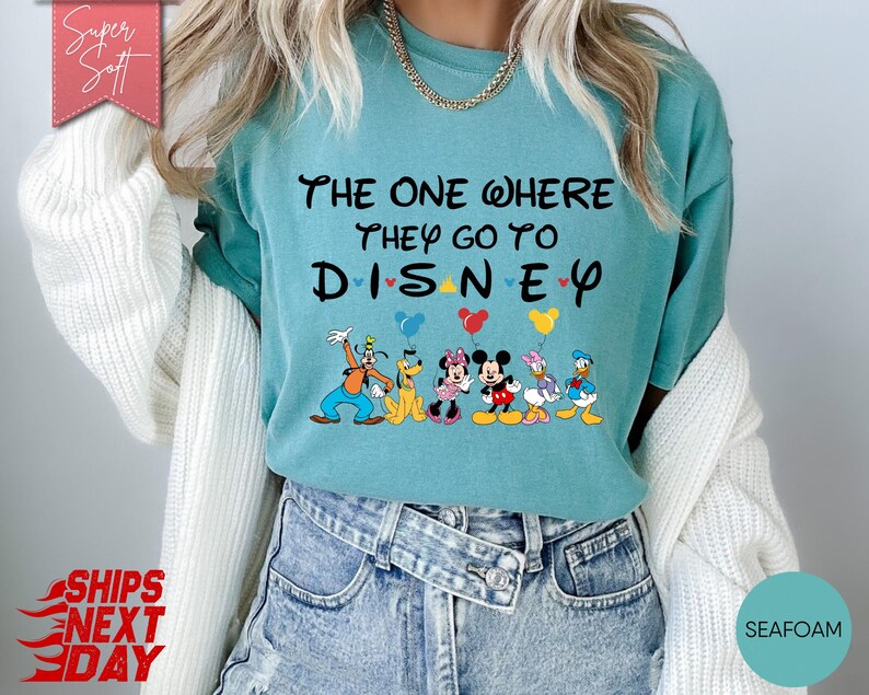 K&ouml;nnte beinhalten: T&uuml;rkisfarbenes T-Shirt mit dem Text "THE ONE WHERE THEY GO TO DISNEY" und Disney-Figuren. Das Shirt zeigt Goofy, Pluto, Minnie Mouse, Mickey Mouse und Donald Duck mit Luftballons. Das Shirt ist aus einem weichen, bequemen Material.