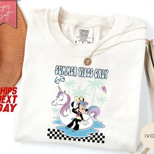 May include: An ivory t-shirt featuring a graphic of a cartoon mouse wearing heart-shaped sunglasses while sitting on a unicorn pool float in water. The text reads SUMMER VIBES ONLY, accompanied by palm trees, sunglasses, and a popsicle graphic.