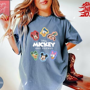 May include: Blue jean colored t-shirt featuring Disney's Mickey and Friends characters. The shirt has a crew neck and short sleeves. The graphic includes Mickey Mouse, Minnie Mouse, Donald Duck, Daisy Duck, Goofy, and Pluto. The text "Mickey and Friends" is printed below the characters.