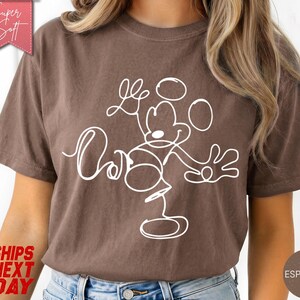 May include: Espresso-colored t-shirt featuring a white line drawing of Mickey Mouse with the word "Love" in cursive. The shirt has a relaxed fit and is made of soft material. The shirt has a vintage look.
